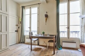 Ein Zimmer mit Holzboden, einem Esstisch mit Stühlen, einer Topfpflanze und einem Heizkörper.