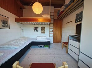 Une pièce de taille modeste, avec deux lits, un plafond en bois, une petite table et un banc.