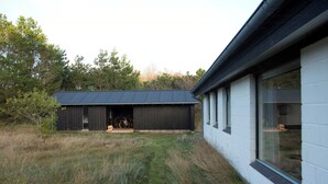 En moderne bygning med et metal tag, et overdækket udendørs område og en hvid facade med store vinduer.