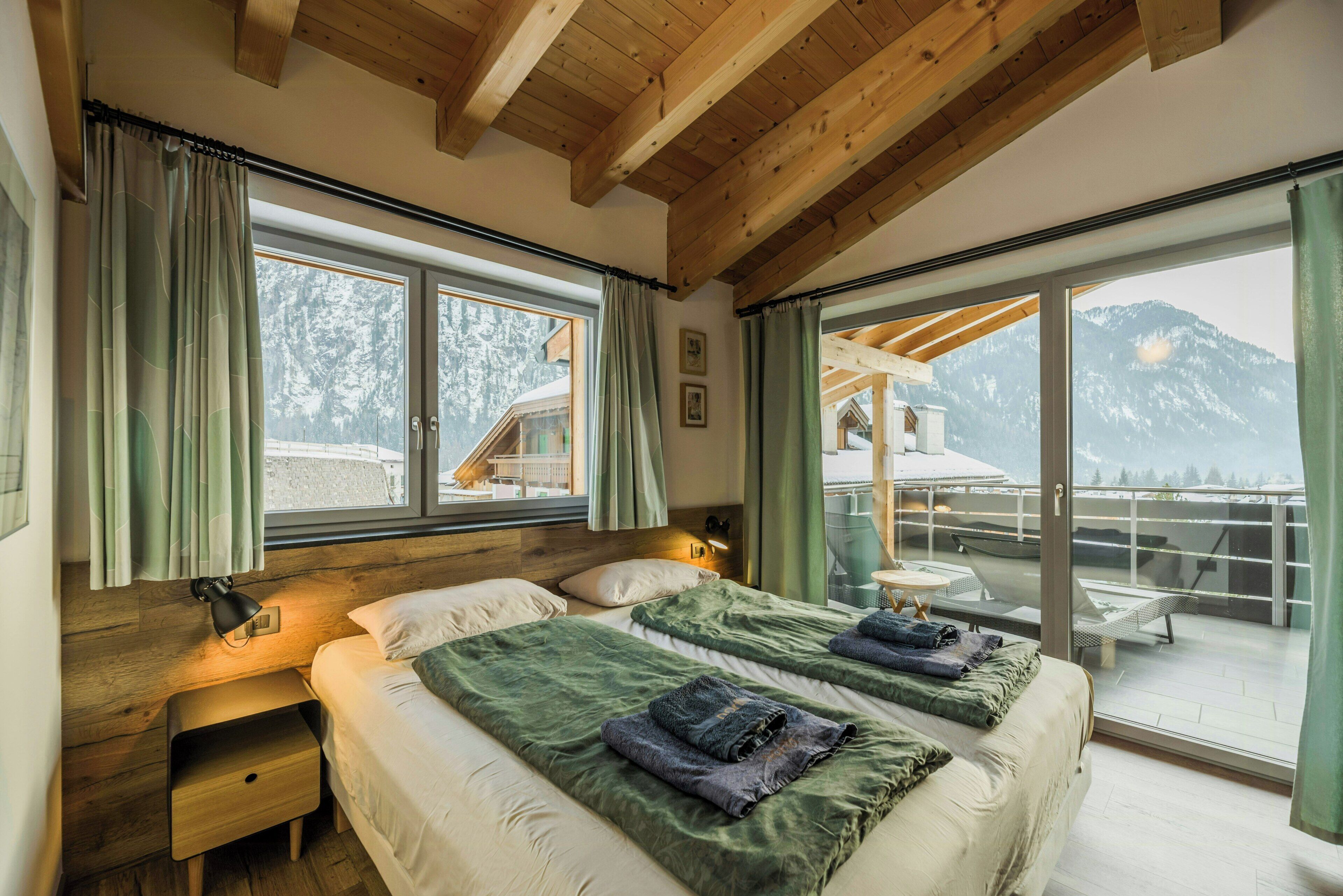 Slaapkamer met twee bedden, houten balken, een balkon met uitzicht op de bergen en een schuifdeur.'