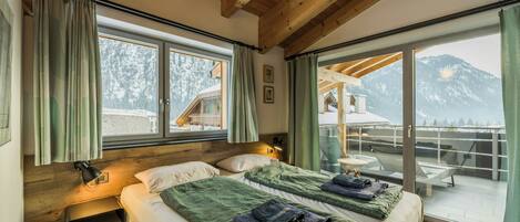 Slaapkamer met twee bedden, houten balken, een balkon met uitzicht op de bergen en een schuifdeur.'