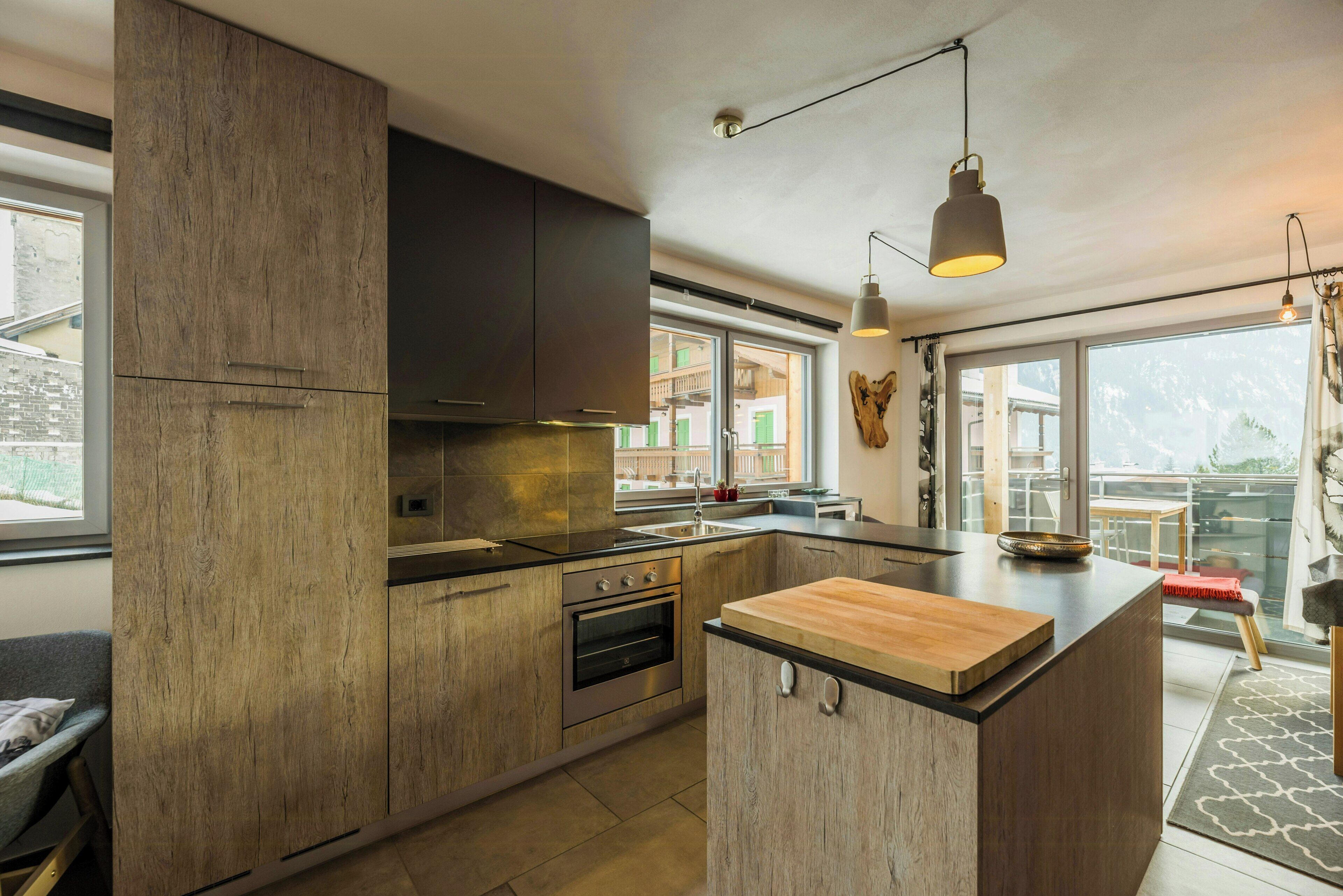 A modern kitchen with wooden cabinetry, a built-in oven, and a large island with a cutting board.
