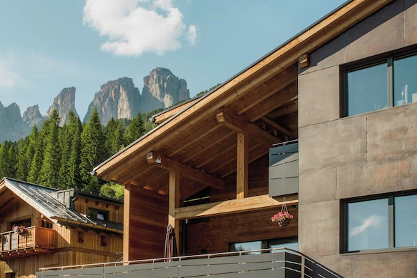 Ein modernes Gebäude mit einem hölzernen Balkon und großen Fenstern vor einer Berglandschaft.