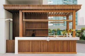 Un mostrador de recepción con detalles de madera, una encimera blanca y vistas a un paisaje urbano a través de amplios ventanales.