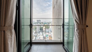 A view from a balcony with a glass railing, overlooking a cityscape with buildings and a clear sky. - Zenity & D1 Mension Apartment by NIDOVA (Ho Chi Minh City)