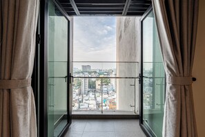 Blick vom Balkon mit Glasgeländer auf eine Stadtlandschaft mit Gebäuden und blauem Himmel.