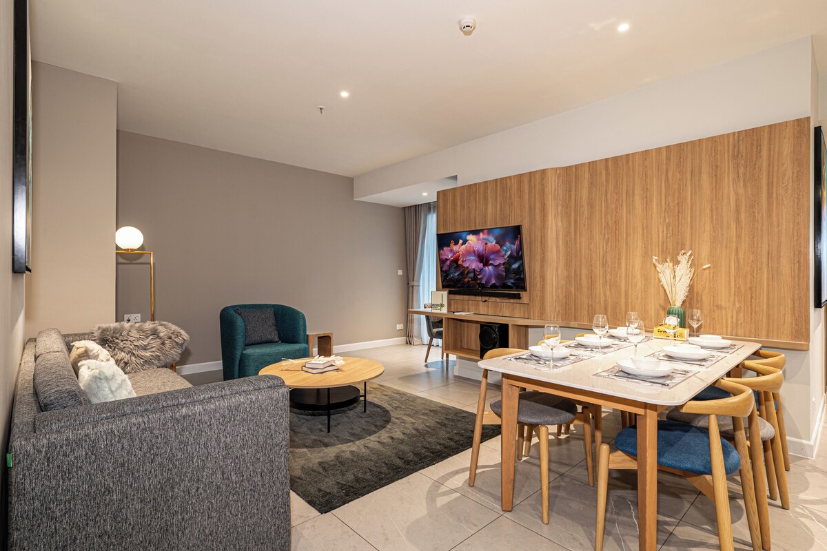 Ein modernes Wohnzimmer mit einer Couch, einem Türkis-farbenen Sessel, einem Couchtisch und einem Essbereich mit einem Holztisch, gedeckt für vier Personen.
