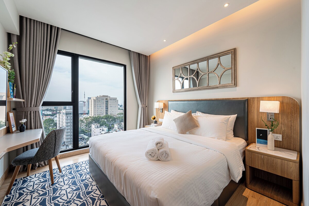 Ein Hotelzimmer mit einem großen Bett, einem Schreibtisch und Blick auf die Stadt.