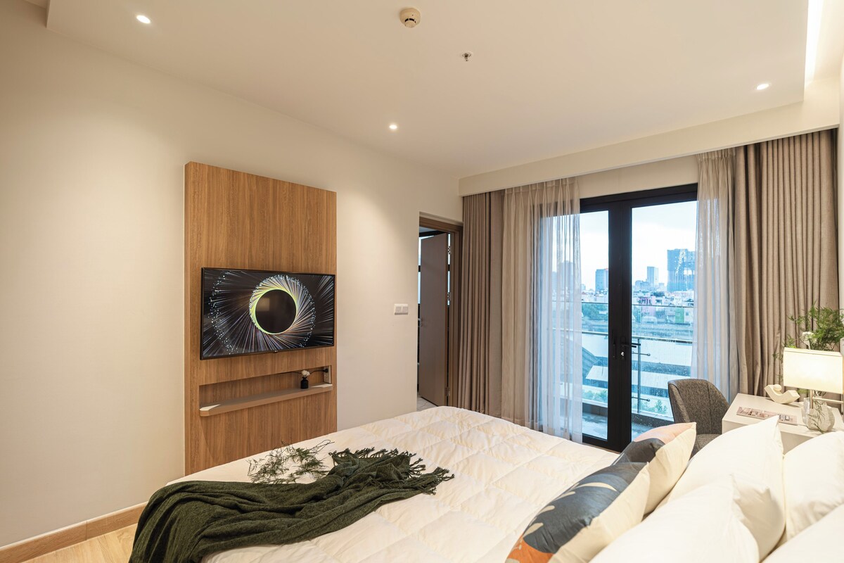 Ein Hotelzimmer mit Bett, einem an der Wand befestigten Kunstwerk, Blick auf die Stadt, einem Sessel und einem Nachttisch mit Lampe.