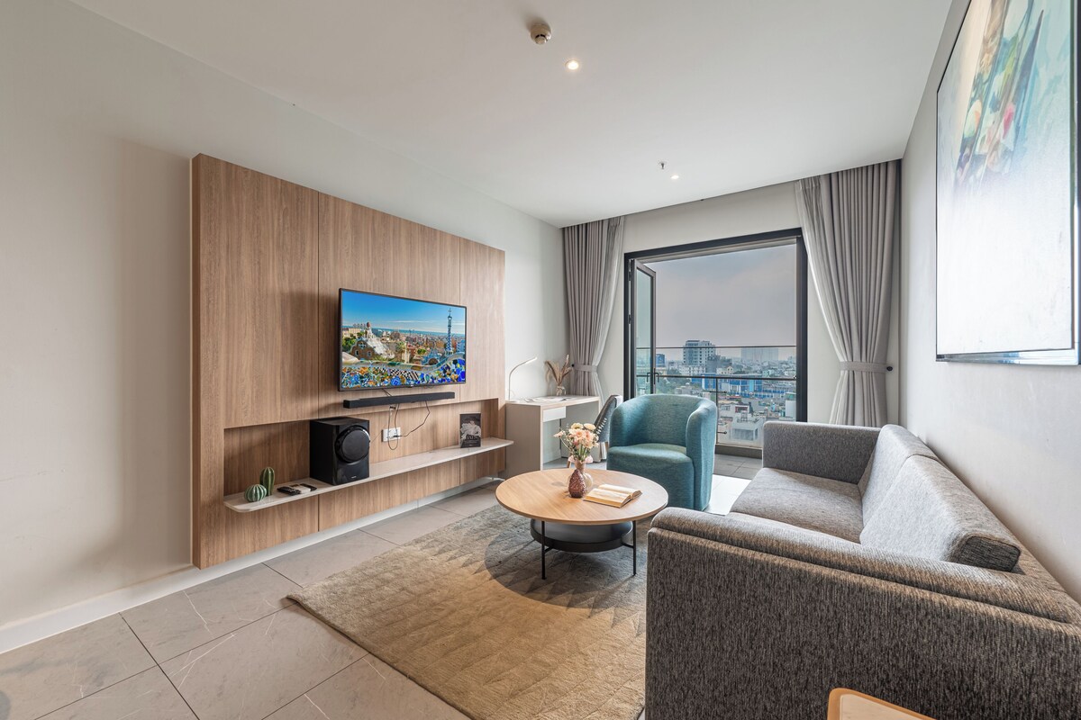 Ein modernes Wohnzimmer mit Fernseher, einer Couch, einem Couchtisch und einem großen Fenster mit Blick auf die Stadt.