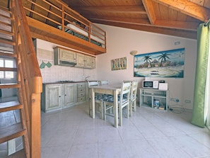 A rustic kitchen with wooden cabinets, a dining table, and chairs. A staircase leads to an upper level. - SOL Bright Apt by the Sea (Santa Maria)