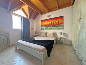 A bedroom with a bed, a nightstand, a lamp, a wardrobe, a painting, and a window with curtains. - SOL Bright Apt by the Sea (Santa Maria)