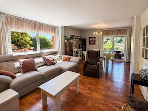 Ein Wohnzimmer mit einer Couch, einem Couchtisch, einem Essbereich mit Tisch und Stühlen sowie einer Küche mit Schränken und einer Pflanze.