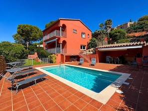 Eine rote Villa mit Swimmingpool, Sitzgelegenheiten im Freien und einem Garten.