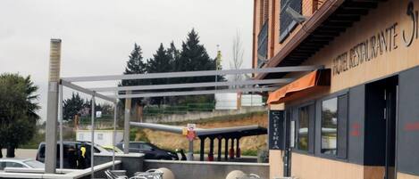 An outdoor seating area with tables and chairs, a building with a sign reading 'HOTEL RESTAURANTE,' and a covered walkway.
