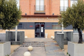 Una entrada de hotel con fachada de ladrillo, puerta de madera y un balcón.