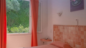 Una habitación con cama, ventana con cortinas, mesita de noche y lámpara de pared.