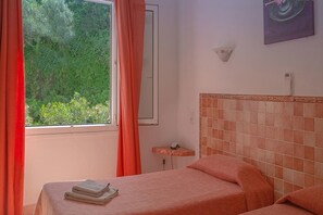 Una habitación con cama, ventana con cortinas, mesita de noche y lámpara de pared.