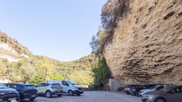 Un estacionamiento con autos, un edificio de techo inclinado y una colina al fondo.