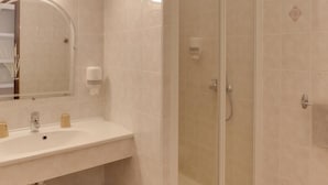 Un baño con lavamanos blanco, espejo y cabina de ducha de vidrio.