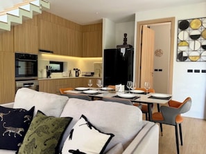 Una sala moderna con un sofá, una mesa de comedor y sillas. Cuenta con una zona de cocina equipada y un refrigerador.