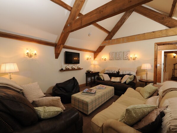 A cozy living room with wooden beams, a flat-screen TV, and a fireplace. - 6 bedroom accommodation in Torrington (Torrington)