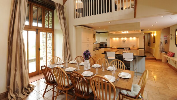 Un coin repas avec des chaises en bois et une table dressée pour six personnes, une cuisine en arrière-plan et un balcon doté d’une balustrade.