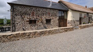 Un bâtiment en pierre avec un toit de chaume, une cheminée et une allée gravillonnée.