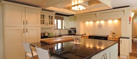 Una cocina con armarios blancos, una isla central, electrodomésticos de acero inoxidable y una zona de comedor con dos sillas.