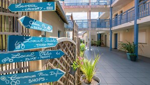 A courtyard with directional signs for amenities like a swimming pool, laundry, trash room, bike room, and shops. - Atlantic Coast Family Apartment (Biscarrosse)