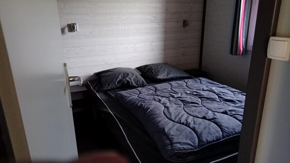 Una habitación pequeña con cama individual, pared de madera, escritorio plegable y cama con cubrecama acolchado.