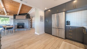 A modern kitchen with dark cabinets, stainless steel appliances, and a wooden dining area.