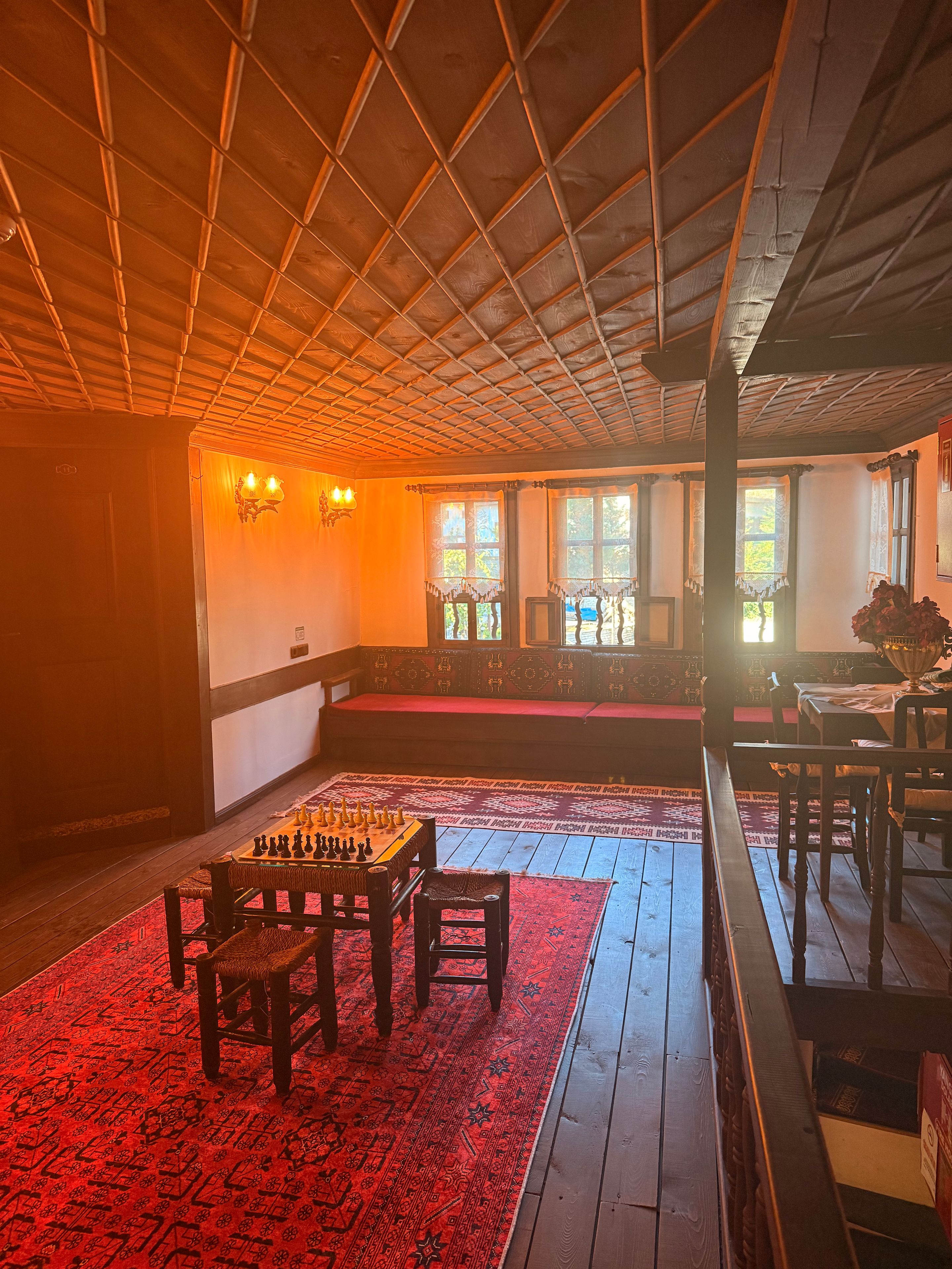 A room with a wooden ceiling, a chessboard on a table, a red patterned rug, and a bench.