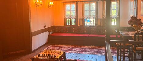 A room with a wooden ceiling, a chessboard on a table, a red patterned rug, and a bench.
