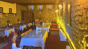 Un restaurante con paredes de piedra, techo de madera y mesas dispuestas con manteles blancos.