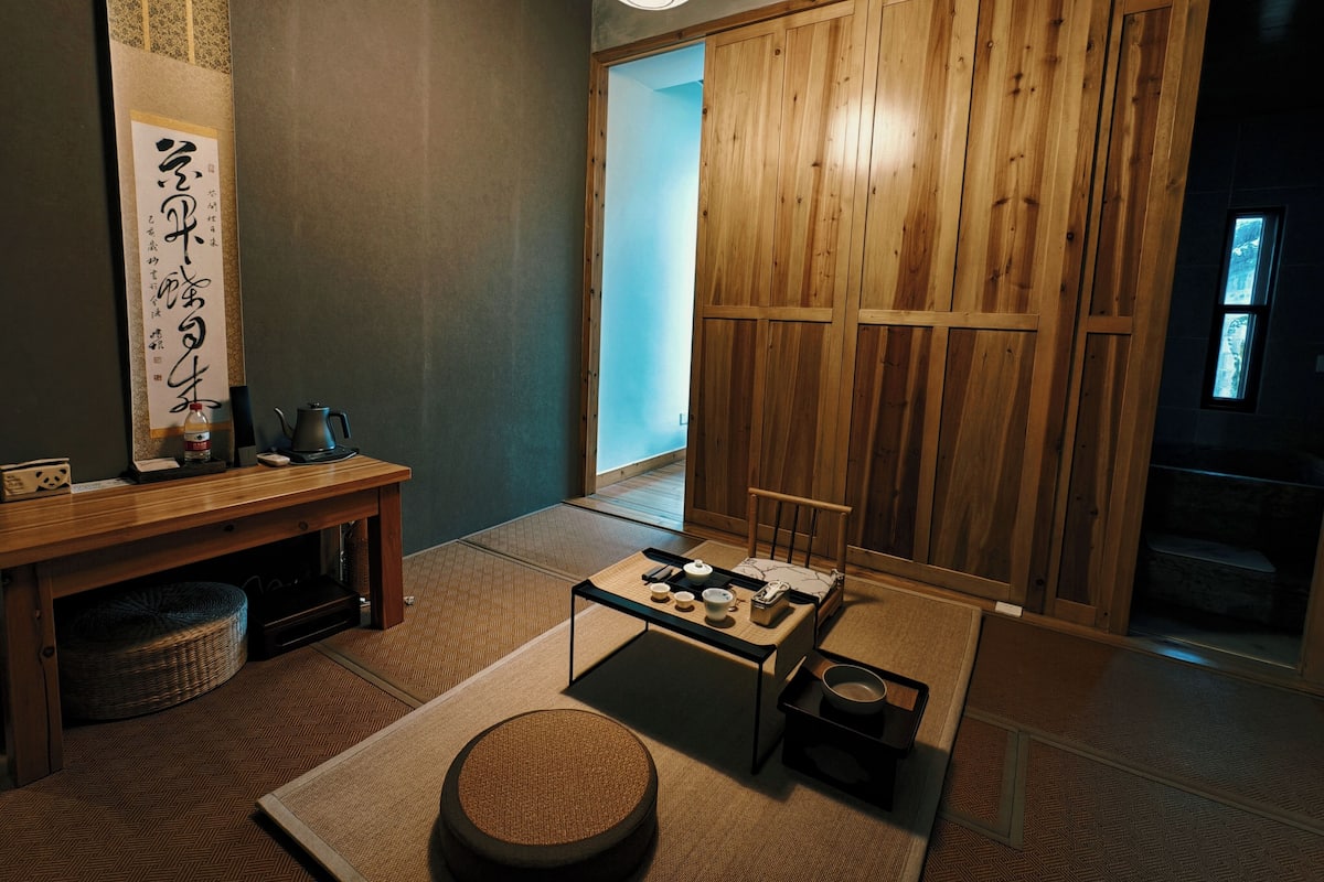 Una habitación japonesa tradicional con suelo de tatami, una mesa baja con utensilios para té, una puerta corredera de madera y un farol colgante.