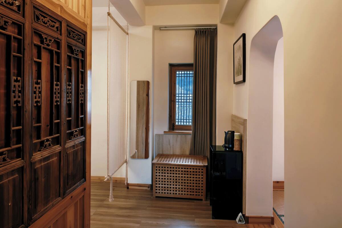 Un pasillo con paneles de madera, un refrigerador negro, una cesta tejida y una ventana con cortinas.