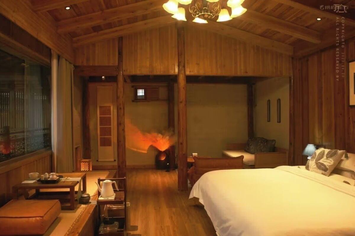 Un interior de madera con una cama, una mesa con una tetera y una chimenea que emite llamas.