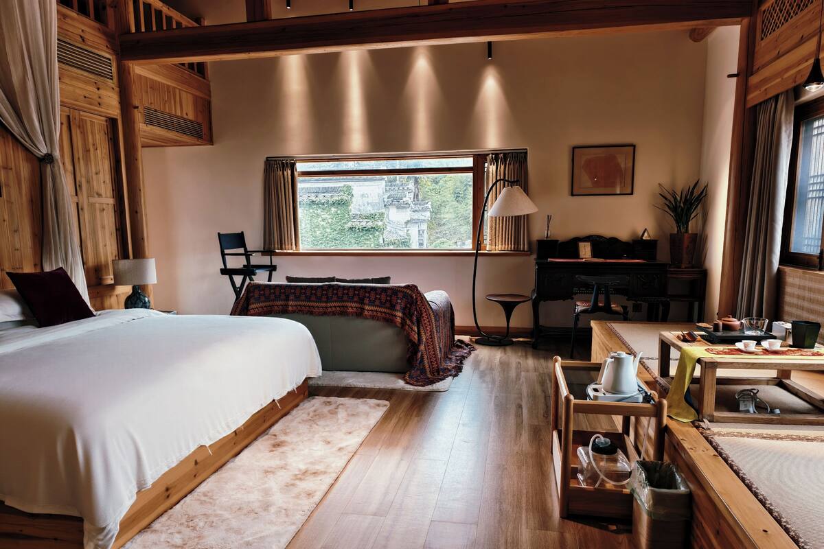 Un dormitorio amplio con una cama grande, un escritorio, una silla y vistas al exterior a través de una ventana.