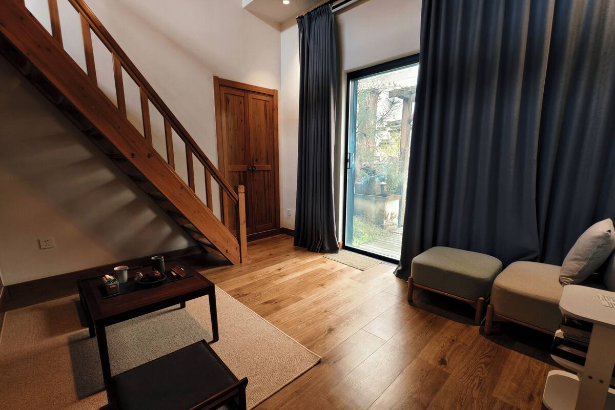 Una sala de estar con una escalera de madera, un sofá, una mesa de centro y un ventanal corredero que da a un balcón.