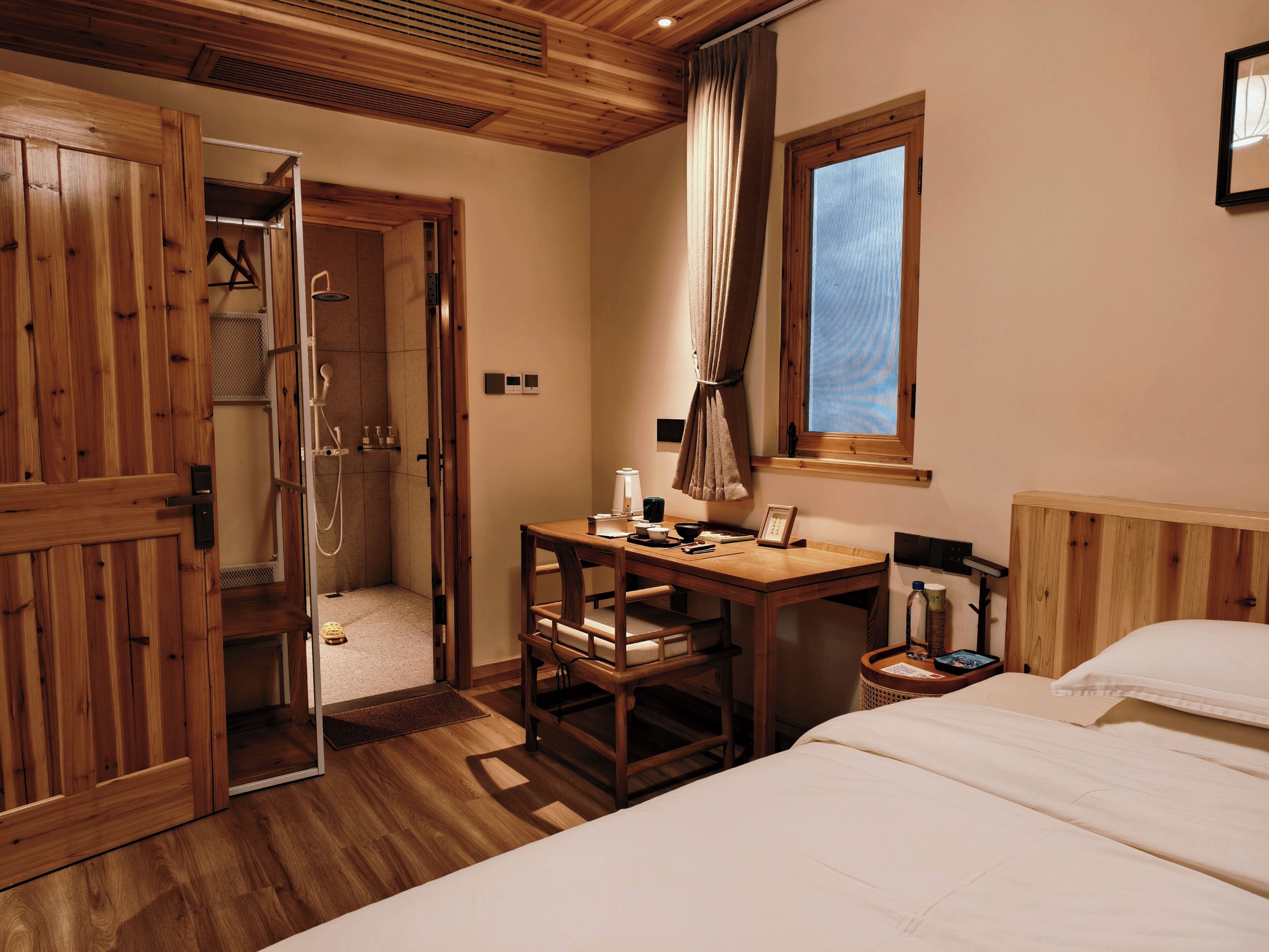 Una habitación de madera con cama, escritorio, ducha y ventana.