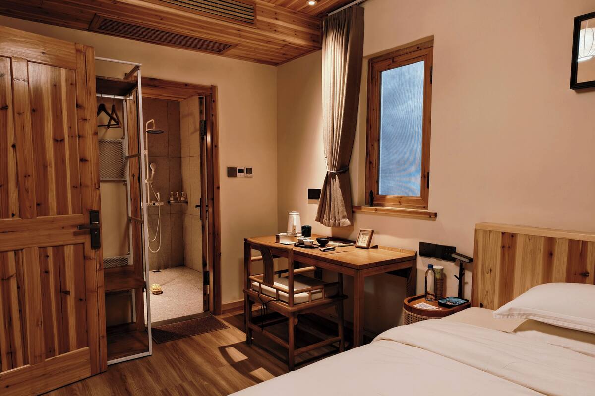 Una habitación de madera con cama, escritorio y zona de ducha.