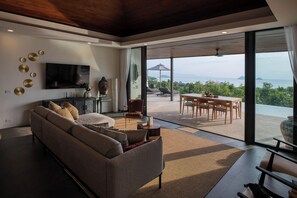 Ein stilvolles Wohnzimmer mit einer Couch, Fernseher und Kunstwerken, das zu einer Terrasse mit Tisch und Stühlen führt.