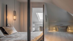 Ein modernes Schlafzimmer mit Bett, Dachfenster, Badewanne und Blick zum Himmel.