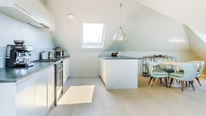 Eine moderne Küche mit integriertem Espressomaschine, einem Essbereich mit rundem Tisch und Stühlen sowie einem großen Fenster, das natürliches Licht hereinlässt.