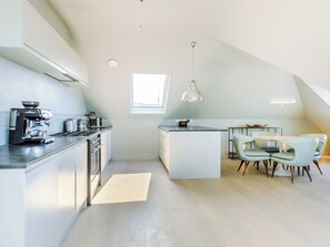 A modern kitchen with a built-in espresso machine, a dining area with a round table and chairs, and a large window providing natural light. - 2 bedroom accommodation in Saunton and Braunton (Saunton and Braunton)