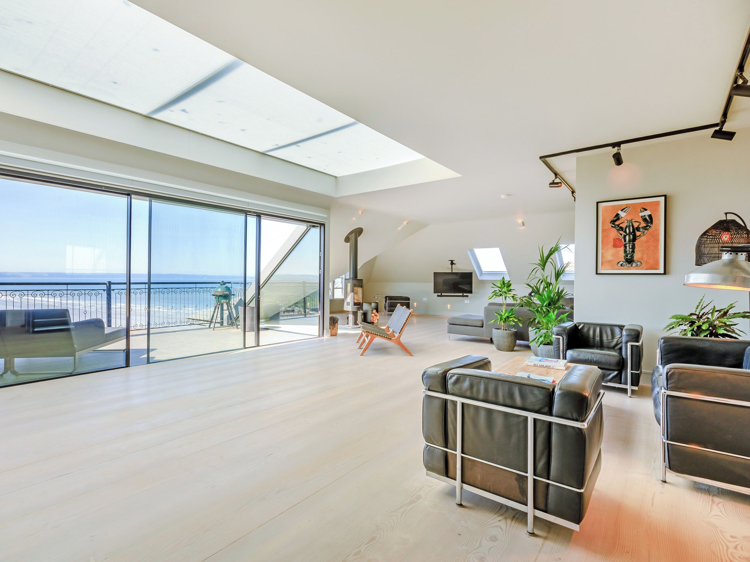 Amplia sala de estar con un balcón grande de vidrio que da al mar, una chimenea moderna y muebles contemporáneos.