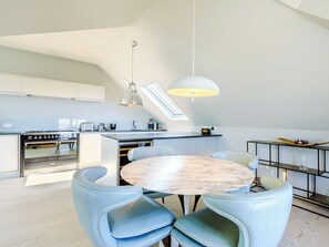 A modern kitchen with a central island, a dining area with a round table and blue chairs, and a skylight above the kitchen. - 2 bedroom accommodation in Saunton and Braunton (Saunton and Braunton)