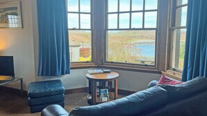 A corner room with a view of the sea, a sofa, a small table, and a lamp. - Plover Apartment - UK51129 (Carradale)