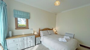 A bedroom with a bed, bedside tables, a dresser, a window with curtains, and a ceiling light fixture. - Plover Apartment - UK51129 (Carradale)